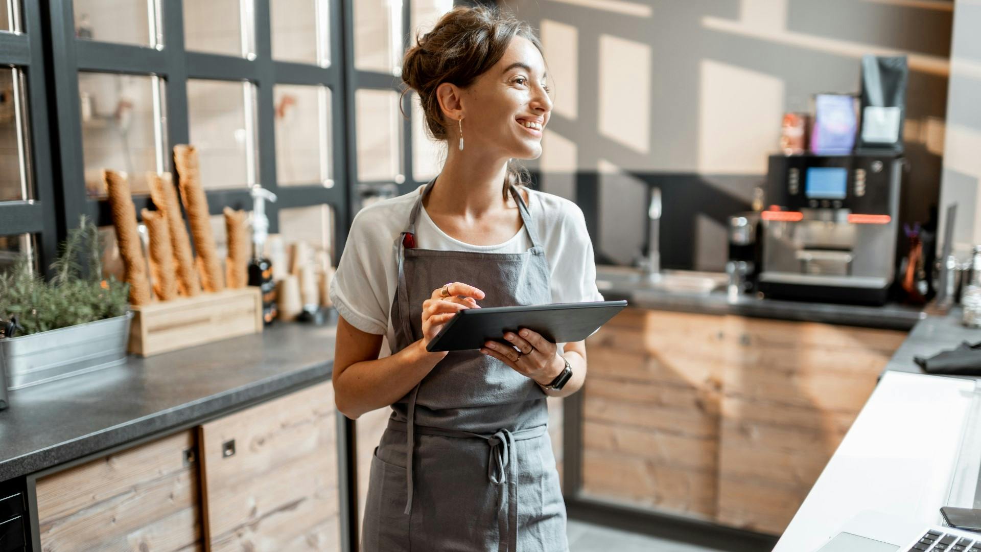 Smiling cashier holding a tablet, looking into the distance